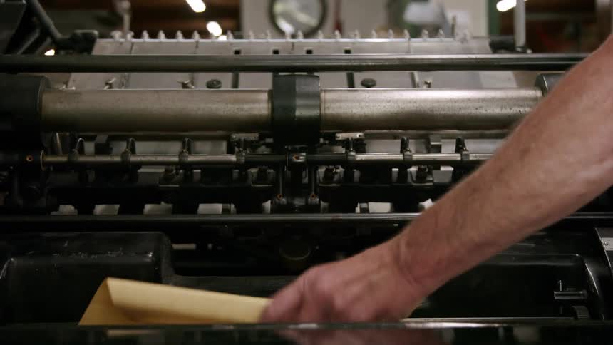 A person feeds paper into a printing press machine