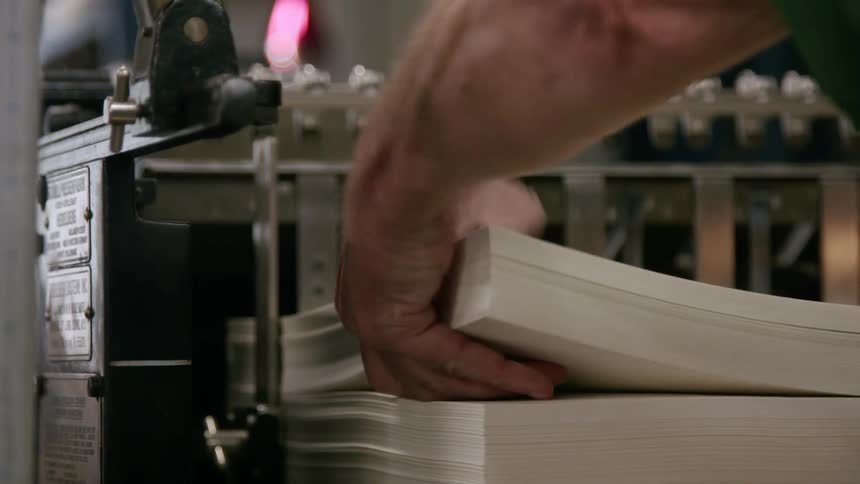 A man flips through the pages of a book beside a printing machine