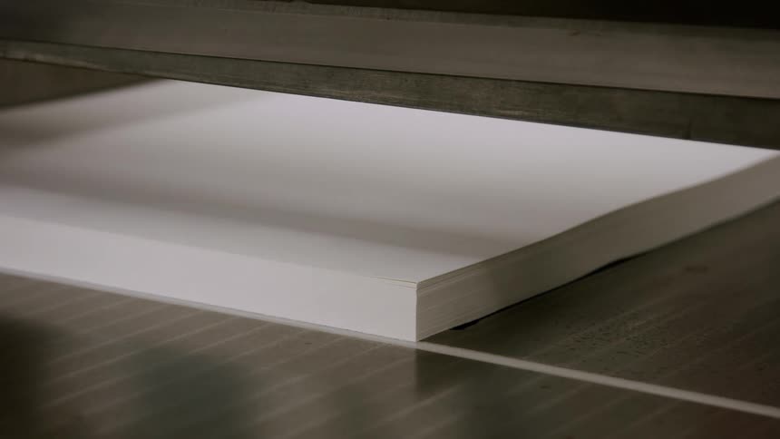 Paper being cut at a die cutting unit and being removed by the hands of a white man indoors