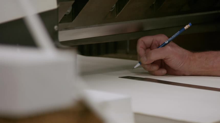Hand marks a line on a sheet with a pencil next to a metal ruler