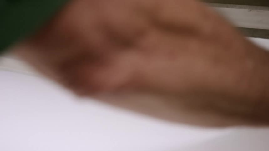A workers hands place a stack of white paper sheets onto a machine and then push them forward into a slot where a dark blade comes down to cut them