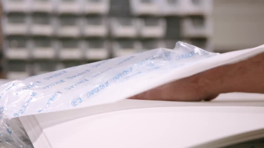 Person handling stacked sheets of paper in a print shop