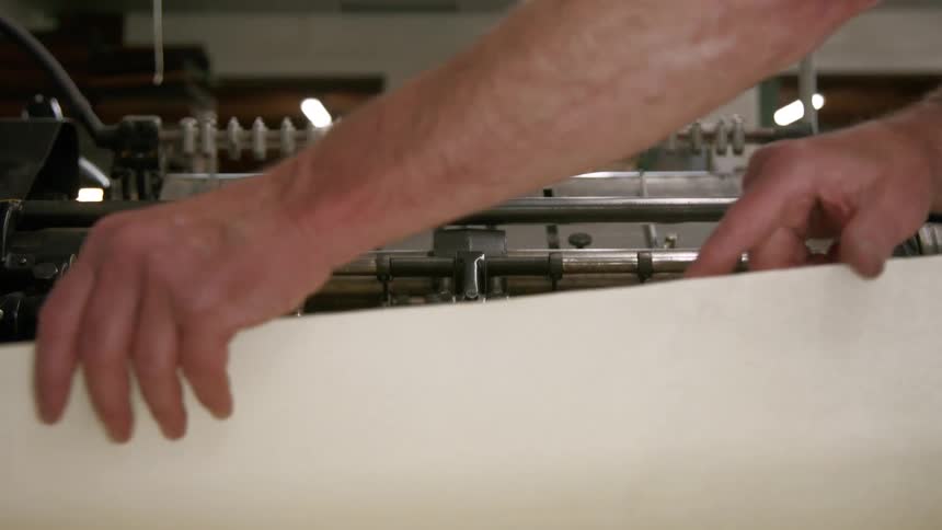 A person places a sheet of paper into a machine and then the machine grabs the paper and pulls it into the press
