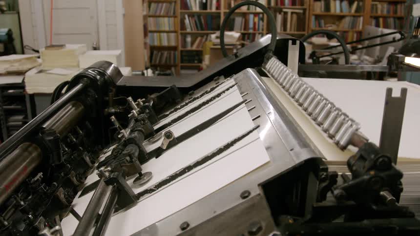 A printing press machine feeds sheets of paper
