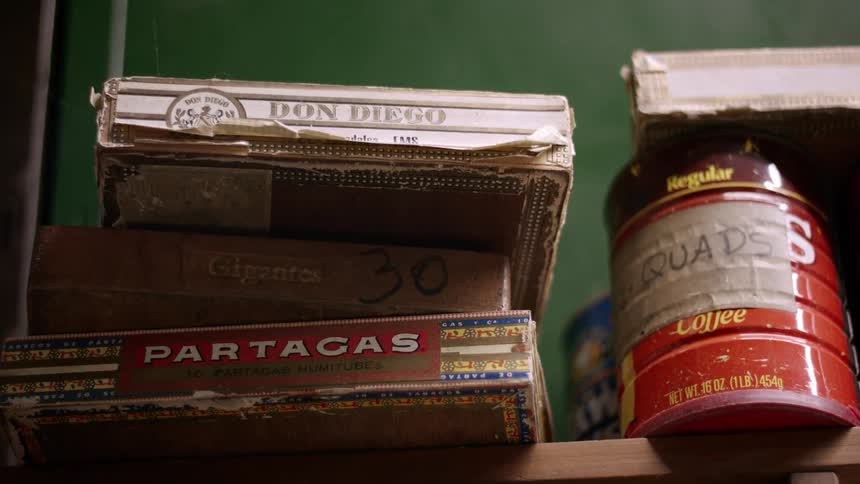 A workshop shelf holds stacked cigar boxes and a labeled coffee can hinting at years of collected parts and tools