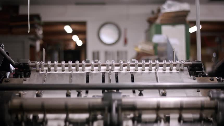 A shot focuses on a vintagestyle printing machine with a line of metal hammers methodically striking a sheet of paper the machine moves with mechanical precision producing printed text with a rhythmic clatter