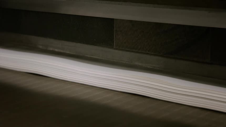 A person feeds paper into a running printing machine in a factory