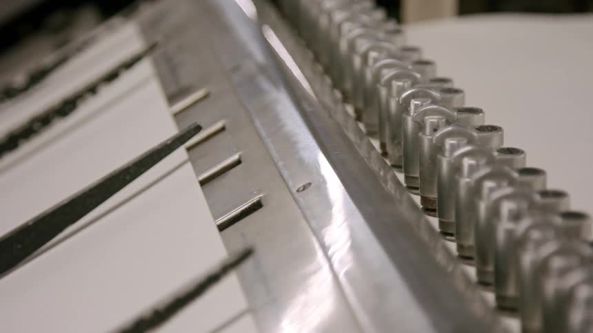 The video shows a closeup shot of a machine in a manufacturing setting with a series of silver metal blades moving rapidly up and down the blades are mounted on a rotating mechanism suggesting a cutting or processing function