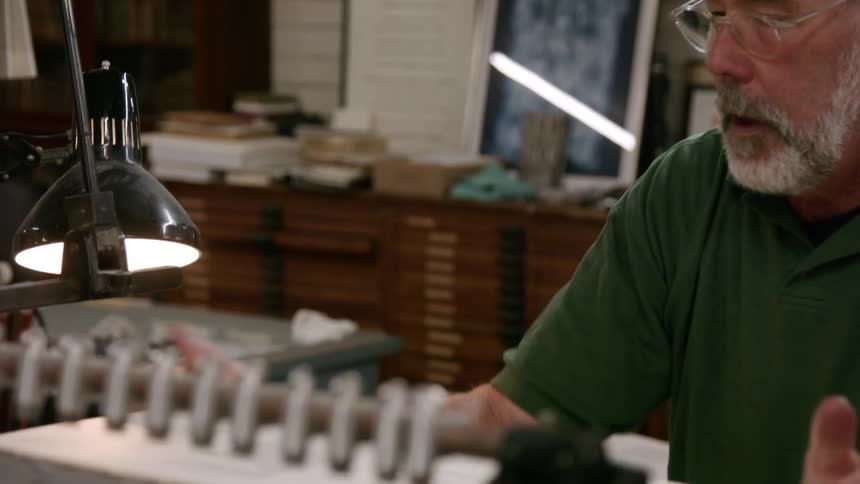The video shows an older man with gray hair and a beard working on a machine the man is wearing a green shirt and glasses and is looking down at the machine while operating it