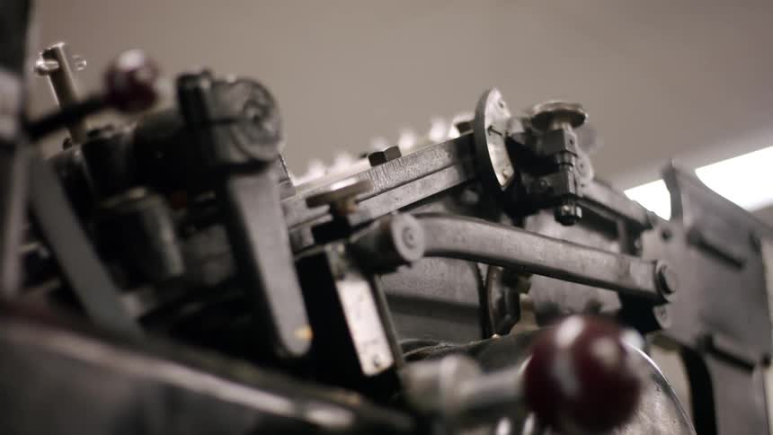 Parts of an older model of mechanical printing press are moving repeatedly