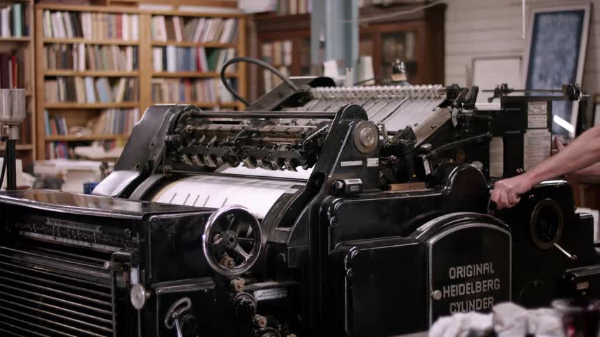An old book printer at work as a man adjusts it