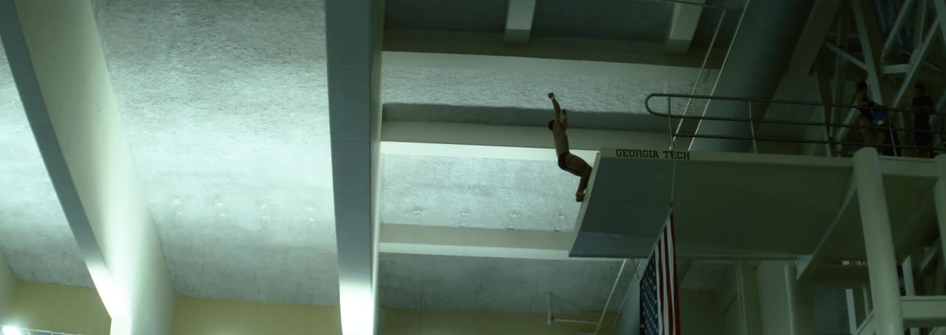 A diver leaps from a high platform in an indoor swimming facility