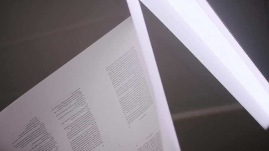 A persons hands are seen holding a large page with black text on it as they examine it against the light