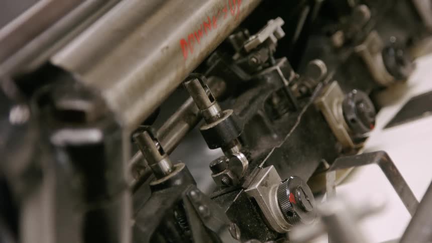 A shot focuses on a vintagestyle printing machine with a line of metal hammers methodically striking a sheet of paper the machine moves with mechanical precision producing printed text with a rhythmic clatter