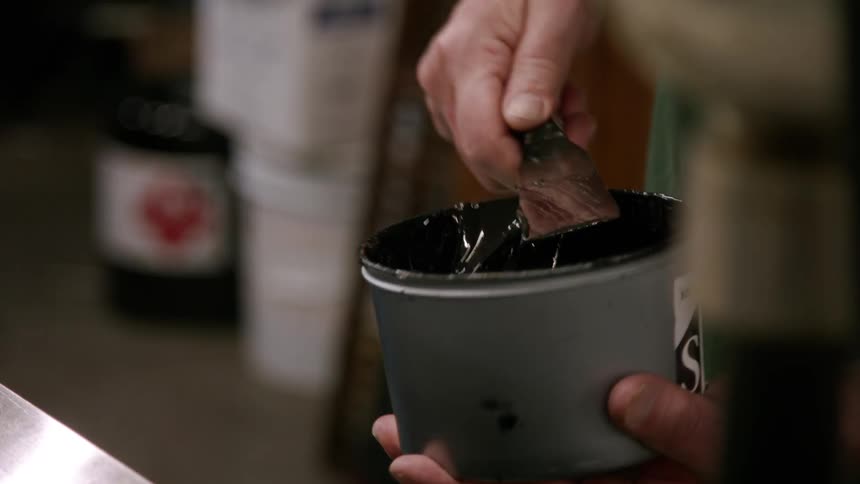 A man scoops a thin layer for resin from a container onto a metal spatula