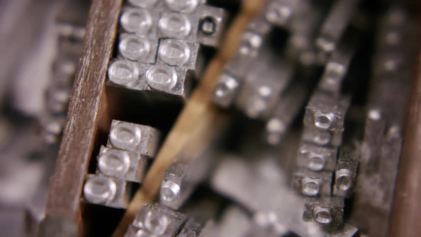 A close view of an open wooden tray with small compartments shows many individual silver metal type letters with a worn texture as the camera slowly zooms in and moves across them