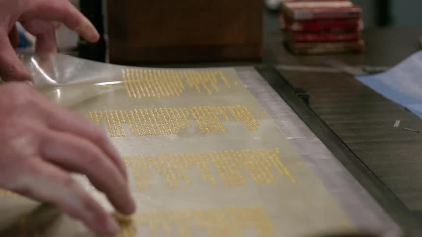A shot focuses on a sheet of plastic with gold lettering that is being peeled away from a metal plate the gold lettering is revealed to be a printed quote as the plastic is slowly pulled back