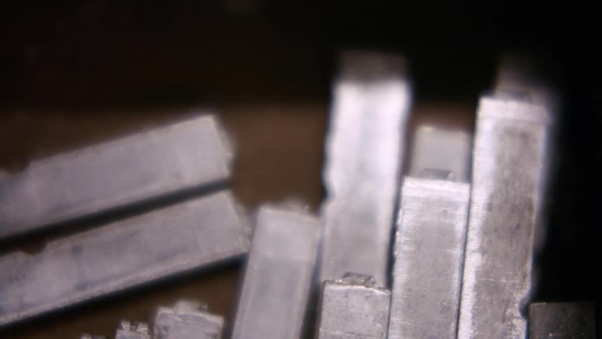 A close view shows the camera slowly panning across several small rectangular pieces of worn grey metal that are piled in a dark space