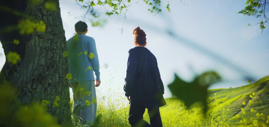 A couple near a tree and a field of grass and yellow flowers