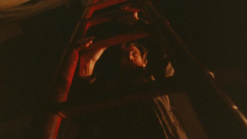 Man climbs a red ladder lit by warm light in a dark setting