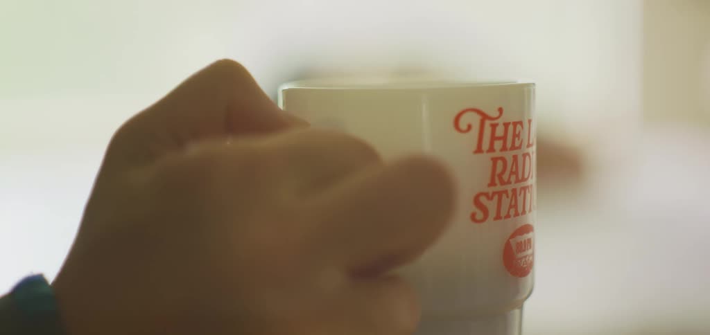 As a person lifts their coffee mug for a drink it reveals a woman facedown
