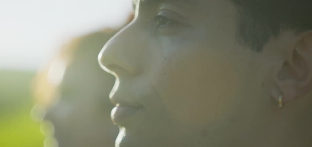A very close view from the side shows a person in the foreground with a woman smiling face coming into focus behind him outdoors