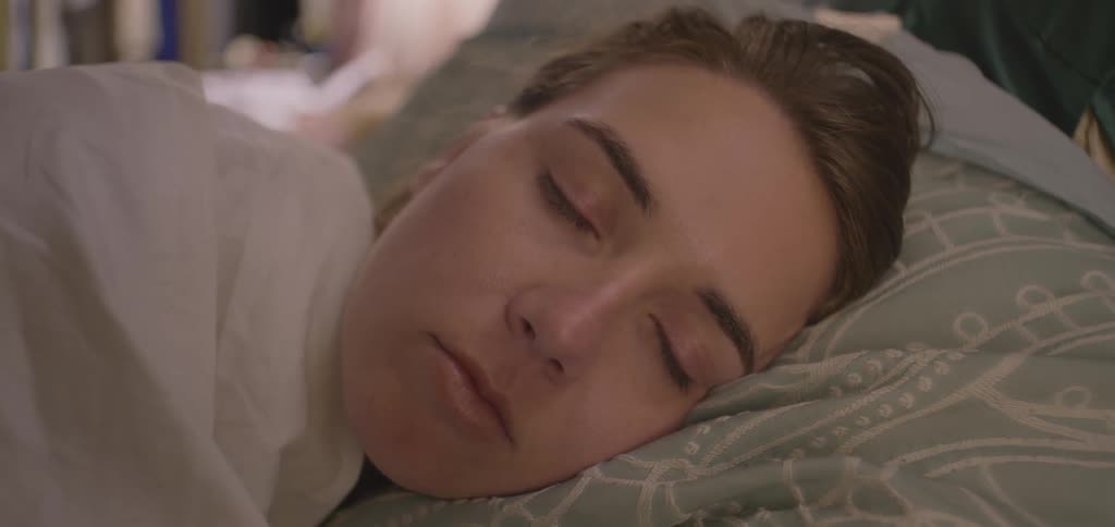 A close view of a woman with her eyes closed as she lies on a pillow with a light geometric pattern