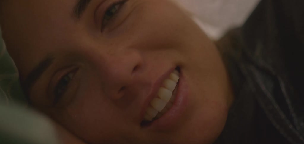 The camera shows a closeup of a womans face as she lies down and smiles