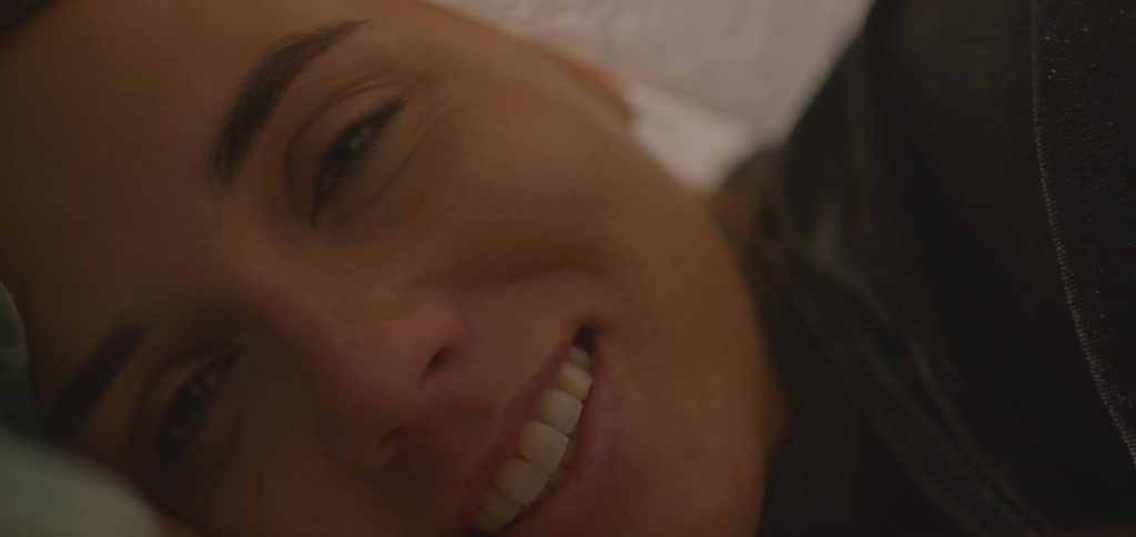 A woman lies on her bed with a smile on her face a blanket draped over her head