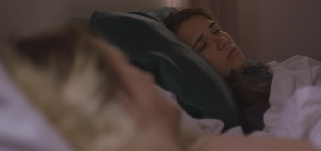 A man and a woman lying in bed with the woman looking at the man sadly