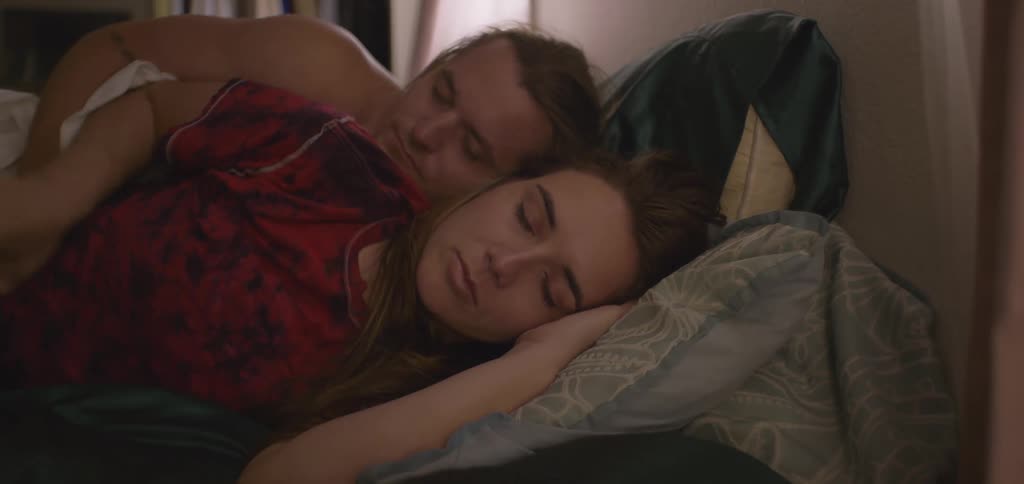 A man rolls over waking up a woman in bed