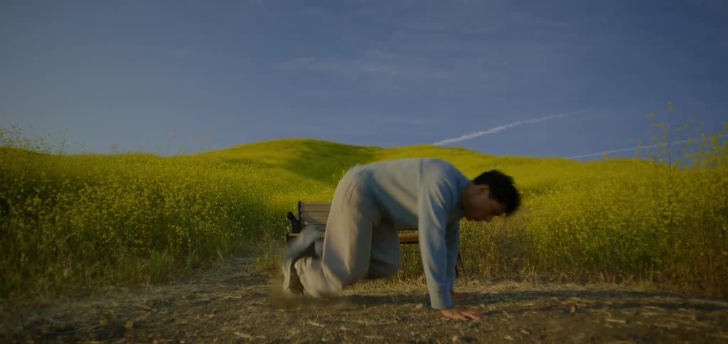 A man dancing outdoors near a bench in the middle of a tall grassy field