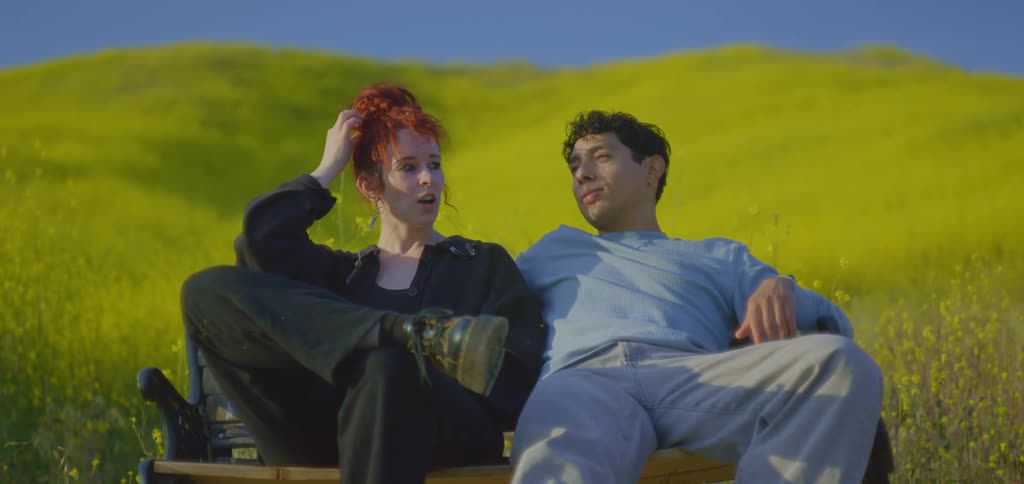 A young man and woman sit for a portrait on a bench near a hill