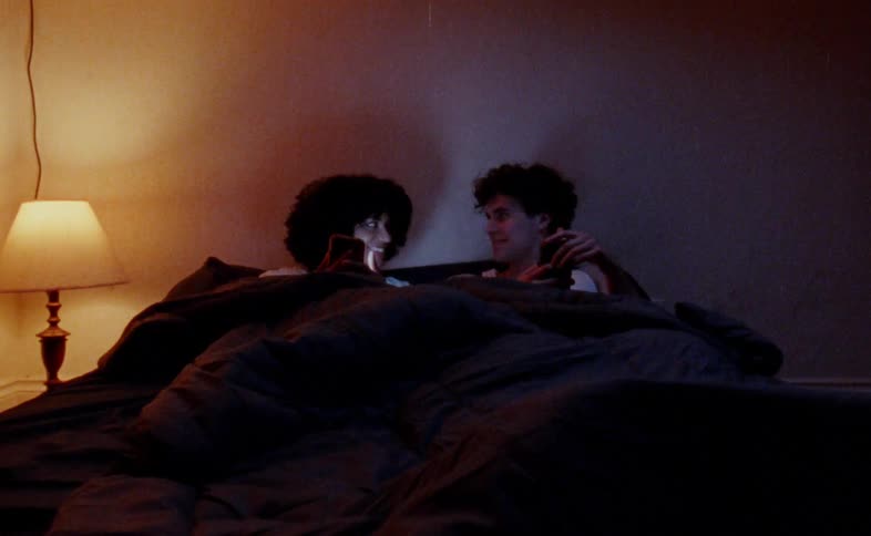 A man and a woman lying in bed using their phones then hugging and covering themselves with a blanket