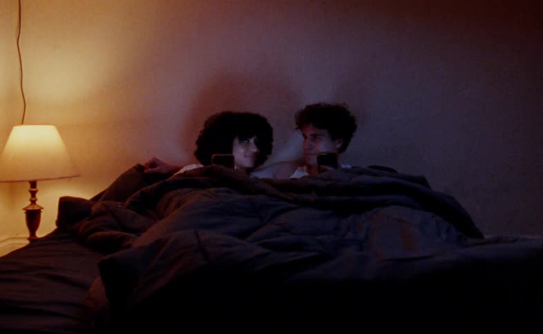 Young couple lying in bed together while looking at their smartphones decides to get amorous and pulls the cover over their heads