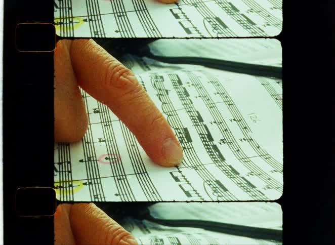A hand points at notes on sheet music framed by vintage film edges