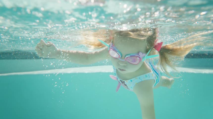 Child swims underwater wearing colorful swimming goggles