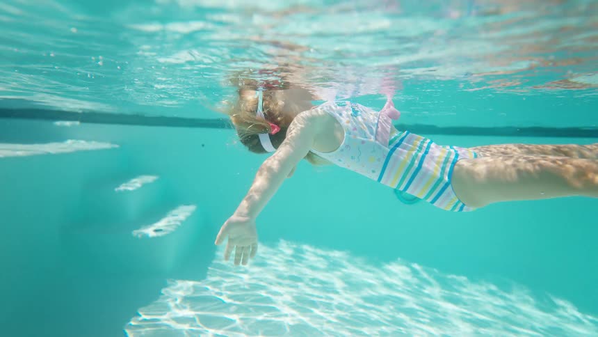 An underwater shot captures a young girl wearing goggles swimming with a peaceful and effortless motion the sunlight filters through the water creating a beautiful and serene environment