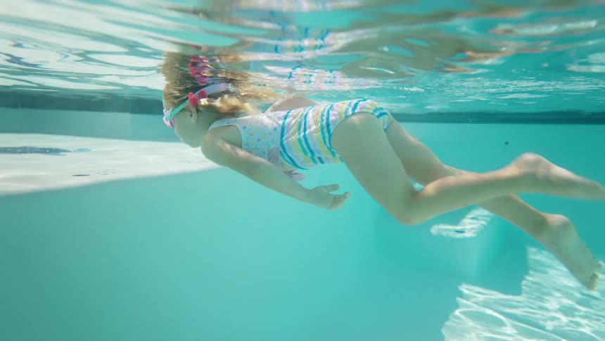 A young girl gracefully swims underwater in a pool