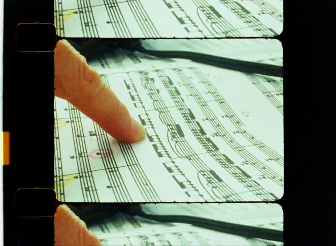 A shot focuses on a persons hand as they gently place their fingers on a sheet of sheet music the frame is stylized with a filmstrip border giving it a vintage look