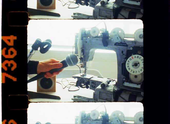 Person holds a microphone close to an industrial sewing machine