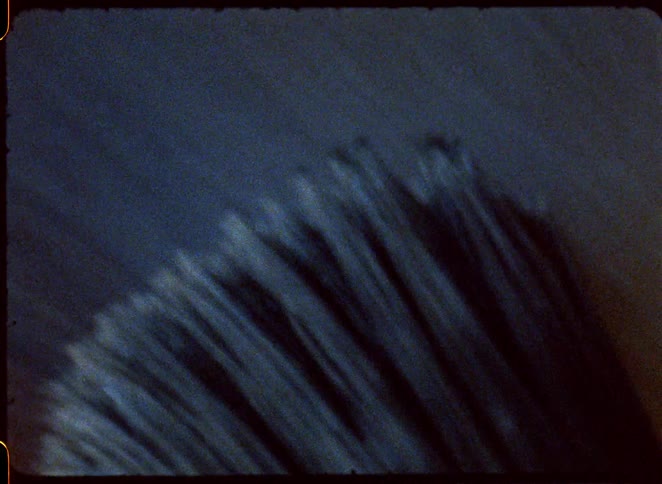 A view through an old film frame with rounded corners shows a quick movement of a dark textured brush spreading paint