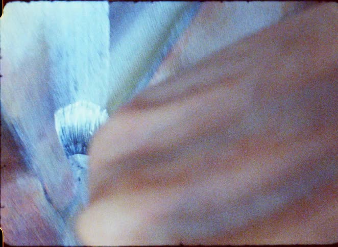 Hand holds a brush applying blue paint on a light surface
