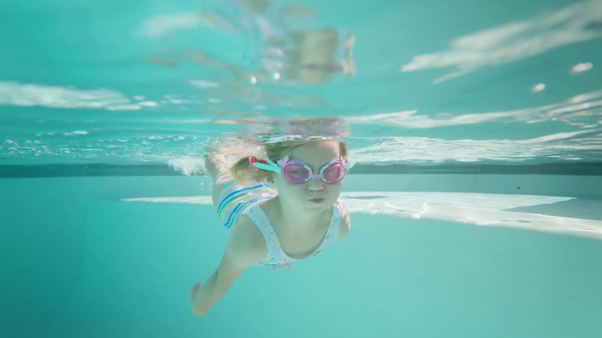 A child wearing goggles swims toward the surface of a pool
