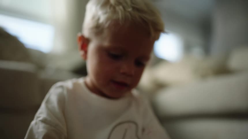 Blond child wears a white shirt while looking down indoors