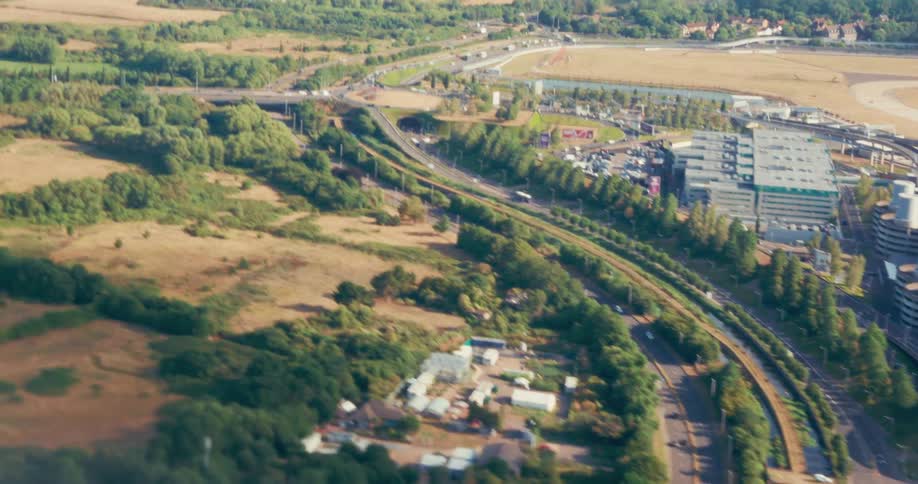 An aerial view shows a landscape of grassy fields trees and buildings next to a busy highway with cars and a winding railway