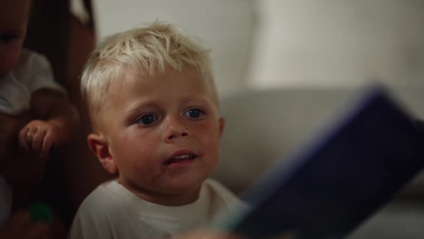 A person holds an infant as the person rubs the head of a boy looking at a book