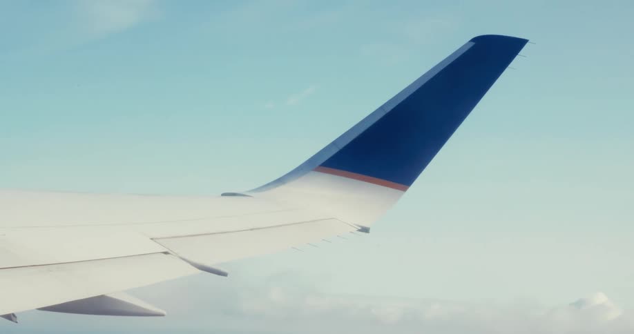 A shot from a plane window captures the wing of the aircraft against a bright blue sky filled with puffy clouds the wing and its bluetipped fin are still and steady against the moving landscape