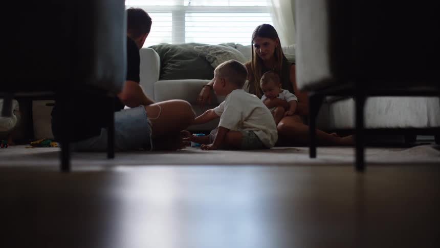 The video shows a family of four including a man a woman and two young children sitting on the floor of a living room the man is seen interacting with one of the children who is holding a toy