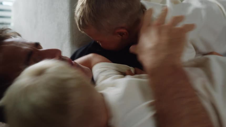 Man lying on the floor plays while hugging two small children